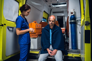 Female paramedic examining an injured man, sitting in an ambulance car