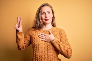 Young beautiful blonde woman wearing casual sweater standing over yellow background smiling...