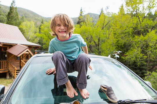 6 year old boy squatting on the front windshield of an SUV in a forest