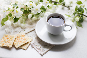 White cup of morning espresso with a blossoming apple tree branch on a stone surface of a table with reflections.