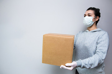 Delivery service worker in gloves and a protective mask on a gray background hands in a parcel. Place for an inscription. Delivery service concept. Infection protection COVID-19