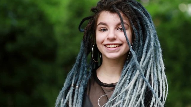 close up portrait of a young pretty smiling woman with dreadlocks, cheerfully looking at the camera walking in city