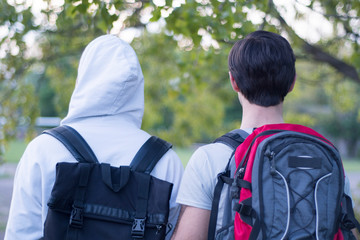 Two friends with tourist backpacks are walking in the forest. Back view