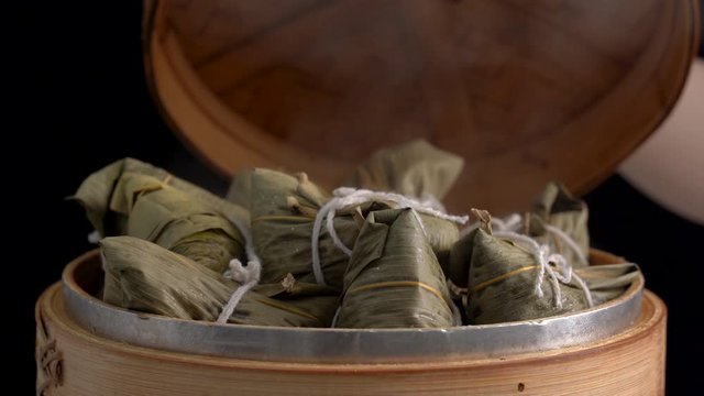 Cooking zongzi - Steamed Chinese rice dumpling in a steamer, fresh prepared food for Dragon Boat Duanwu Festival isolated on black background, close up lifestyle.
