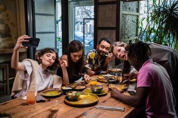 Five young friends sitting at the table in a cafe, taking selfie