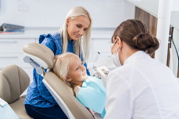 Fototapeta premium Dentysta czyści zęby dziewczynie specjalnym narzędziem, dziewczynka patrzy na lekarza