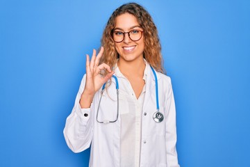 Young beautiful blonde doctor woman with blue eyes wearing coat and stethoscope smiling positive doing ok sign with hand and fingers. Successful expression.