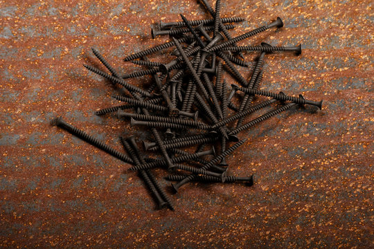 Pu&ntilde;ado de tornillos negros sobre una lamina metalica oxidada.
