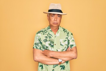 Middle age senior grey-haired man wearing summer hat and floral shirt on beach vacation skeptic and nervous, disapproving expression on face with crossed arms. Negative person.