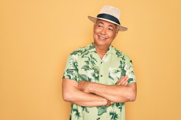 Middle age senior grey-haired man wearing summer hat and floral shirt on beach vacation looking away to side with smile on face, natural expression. Laughing confident.