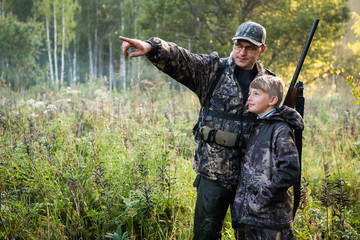 Father teaching his son about gun safety and proper use on hunting in nature. - 347999774
