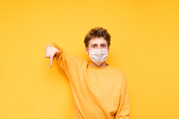 Emotional young man in bright clothes points his finger down at the copy space and looks at the camera with a shocked face, isolated on an orange background. Coronavirus pandemic. Quarantine. covid-19