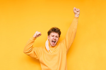 Portrait of a joyful guy with a removed medical mask on a yellow background, a man rejoices at the...