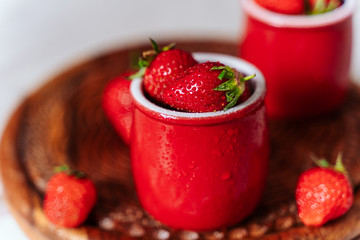 fresh strawberries in red pots on a wooden background, on a drop of water berries. healthy nutrition, vitamin charge, summer berries