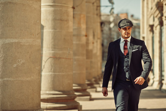 Portrait of retro 1920s english arabian business man wearing dark suit, tie and flat cap near old columns.