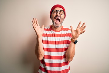 Middle age hoary man wearing striped t-shirt glasses and cap over isolated white background celebrating mad and crazy for success with arms raised and closed eyes screaming excited. Winner concept