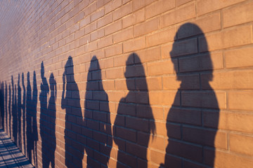 People crowd shadows lined up against a red brick wall. They are in a queue for changes in life. Social distance, covid and immigration issue concept - obrazy, fototapety, plakaty