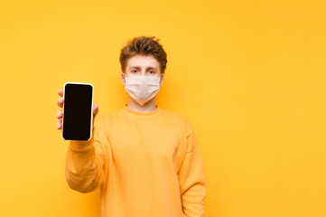 Handsome guy in a yellow sweatshirt and a protective gauze mask stands on an orange background and...
