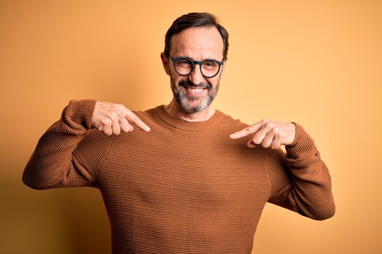 Middle age hoary man wearing brown sweater and glasses over isolated yellow background looking confident with smile on face, pointing oneself with fingers proud and happy. - Powered by Adobe