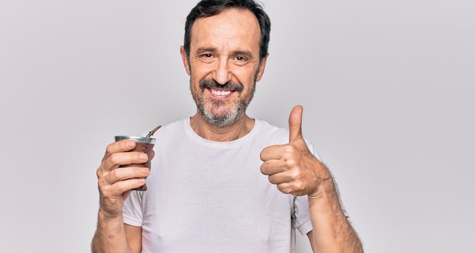 Middle age handsome man drinking cup of mate tea over isolated white background smiling happy and positive, thumb up doing excellent and approval sign