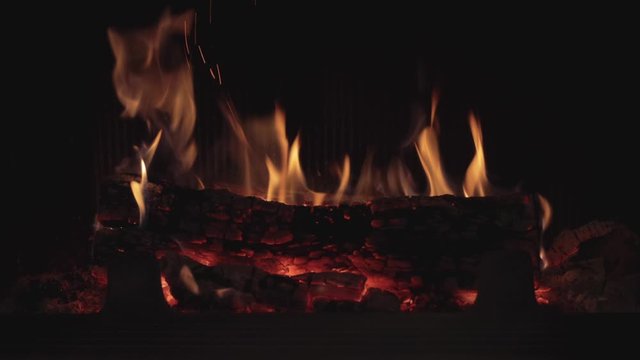 Dark still shot of a firepalce burning with red hot wood logs and black walls, medium close up still shot