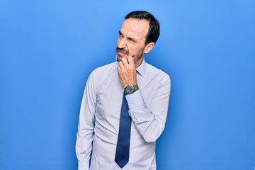 Middle age handsome business man wearing elegant tie standing over isolated blue background thinking concentrated about doubt with finger on chin and looking up wondering