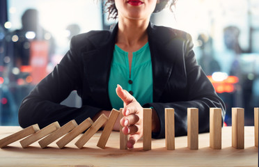 Businesswoman stops a chain fall like domino game. Concept of preventing crisis and failure in...