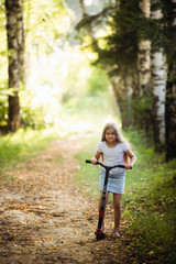 Little girl running scooter in summer forest