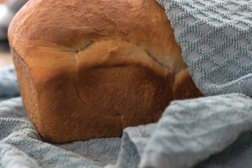 A freshly baked loaf of white sandwich bread wrapped up in a towel to keep warm.