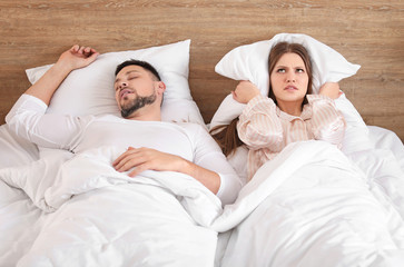 Young irritated woman in bed with snoring husband at home