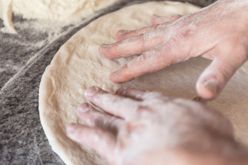 Fototapeta na wymiar Stendere l'impasto della pizza con le mani con metodo artiginale