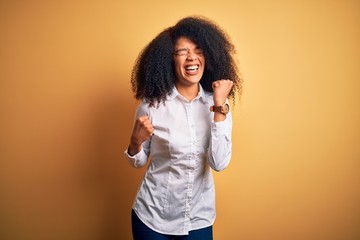 Young beautiful african american elegant woman with afro hair standing over yellow background celebrating surprised and amazed for success with arms raised and eyes closed. Winner concept.