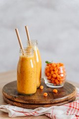 Bright sea buckthorn smoothie on a rustic board. berries, ginger, glass bottles, paper tubes. no plastic. healthy food