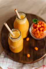 Bright sea buckthorn smoothie on a rustic board. berries, ginger, glass bottles, paper tubes. no plastic. healthy food