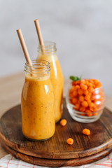 Bright sea buckthorn smoothie on a rustic board. berries, ginger, glass bottles, paper tubes. no plastic. healthy food