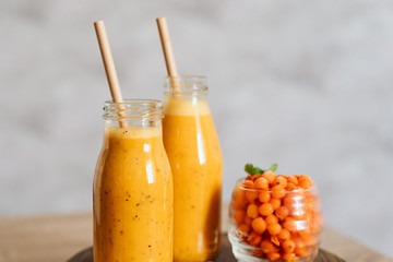 Bright sea buckthorn smoothie on a rustic board. berries, ginger, glass bottles, paper tubes. no...