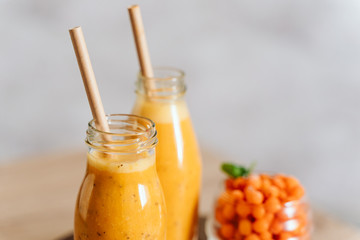 Bright sea buckthorn smoothie on a rustic board. berries, ginger, glass bottles, paper tubes. no plastic. healthy food