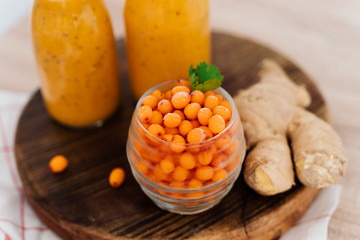 Bright sea buckthorn smoothie on a rustic board. berries, ginger, glass bottles, paper tubes. no plastic. healthy food