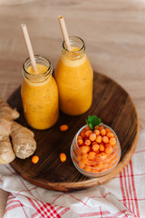 Bright sea buckthorn smoothie on a rustic board. berries, ginger, glass bottles, paper tubes. no plastic. healthy food
