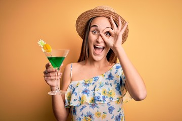 Young beautiful tourist woman on vacation wearing summer hat drinking cocktail beverage with happy face smiling doing ok sign with hand on eye looking through fingers