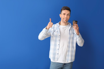 Handsome man with coffee showing thumb-up on color background