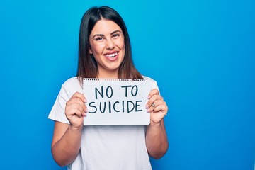 Fototapeta na wymiar Young beautiful woman asking for psychical problem holding paper with not to suicide message looking positive and happy standing and smiling with a confident smile showing teeth