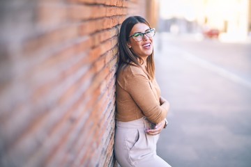 Young beautiful woman smiling happy and confident. Standing with smile on face leaning on the wall at the town street