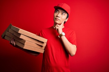 Young handsome chinese delivery man holding deliver boxes with Italian pizza serious face thinking...
