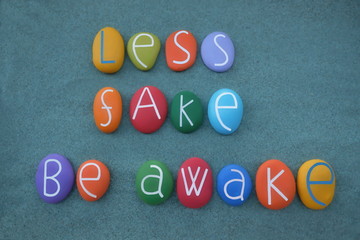 Less fake, Be awake, creative slogan composed with multi colored stone letters over green sand
