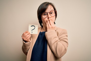 Young down syndrome business woman holding question mark paper as doubt symbol cover mouth with hand shocked with shame for mistake, expression of fear, scared in silence, secret concept