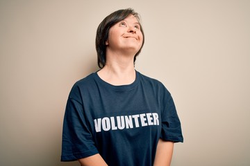 Young down syndrome volunteer woman wearing social care charity t-shirt looking away to side with smile on face, natural expression. Laughing confident.