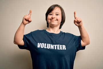 Young down syndrome volunteer woman wearing social care charity t-shirt smiling amazed and...