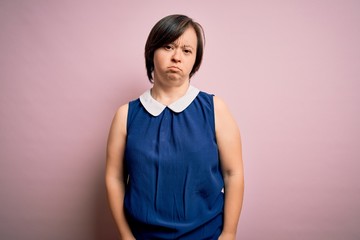 Young down syndrome woman wearing elegant shirt over pink background with serious expression on face. Simple and natural looking at the camera.