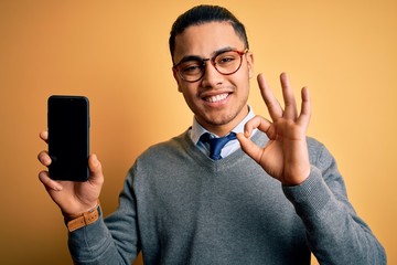 Young brazilian businessman wearing glasses holding smartphone showing screen doing ok sign with fingers, excellent symbol